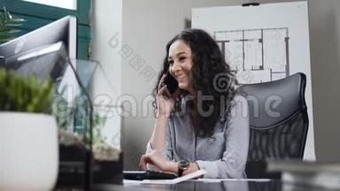 卷发女<strong>建筑</strong>师在智能<strong>手机</strong>上交谈，并在工作<strong>日</strong>在办公室微笑。
